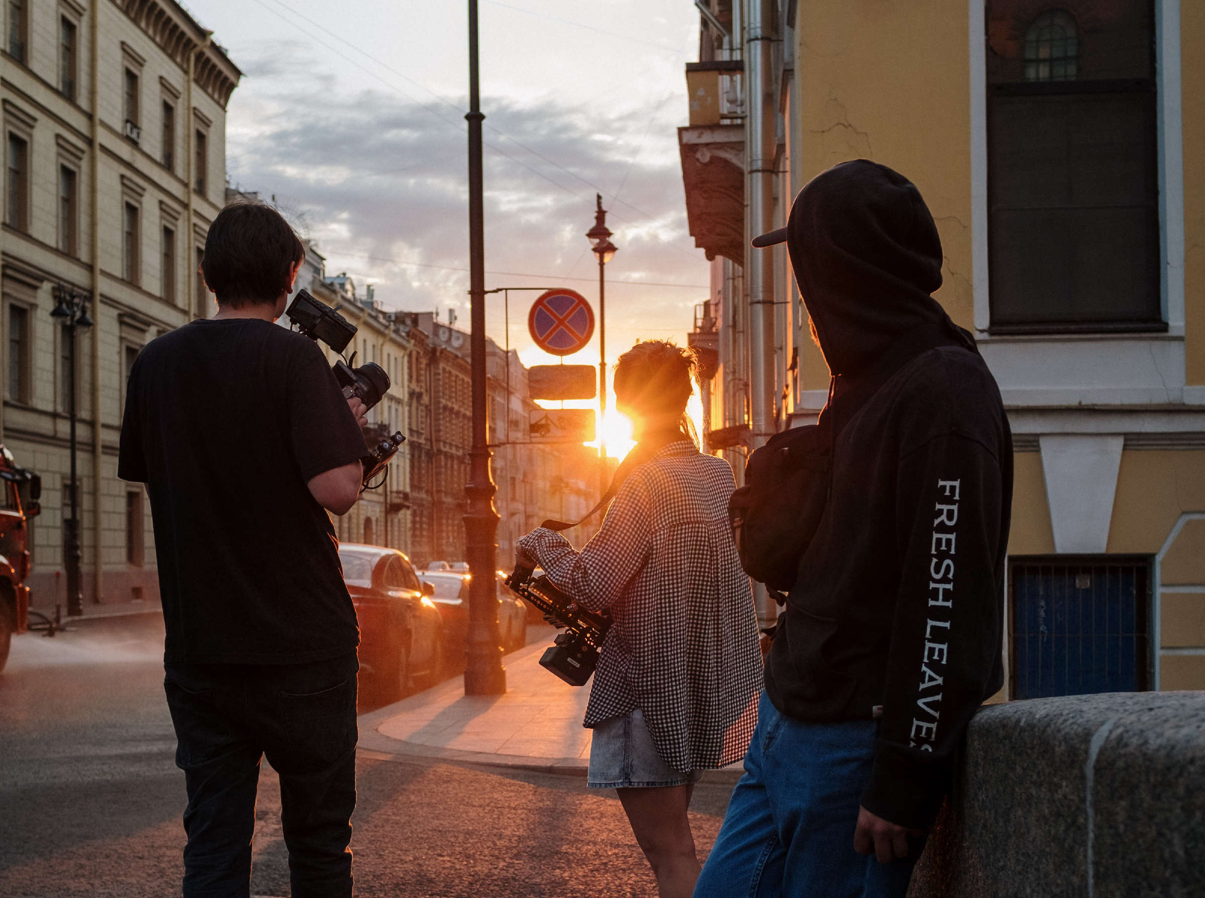 Drei Jugendliche stehen mit Kameras auf dem Bürgersteig